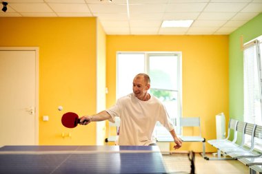 Beyaz tişörtlü bir adam masa tenisi oynamaktan hoşlanır. Pinpon kulübünde dostça bir rekabet.