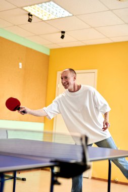 Beyaz tişörtlü bir adam masa tenisi oynamaktan hoşlanır. Pinpon kulübünde dostça bir rekabet.