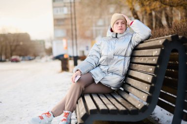 Kışın parkta yürürken akıllı telefon ve cep telefonu kullanan beyaz bir kızın portresi.