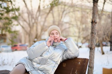 Kafkasyalı genç bir kızın portresi. Akıllı telefon kullanıyor. Kışın parkta cep telefonuyla konuşuyor.