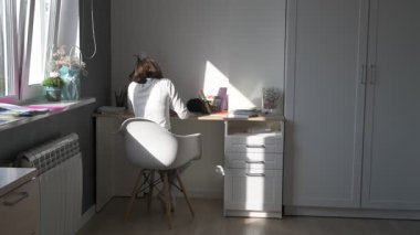 Evde eğitim gören liseli kız. Kız ders kitaplarıyla masada oturup ödev yapıyor.