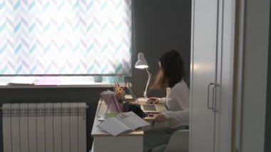 Evde eğitim gören liseli kız. Kız ders kitaplarıyla masada oturup ödev yapıyor.