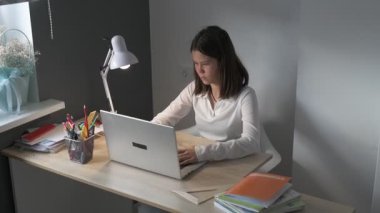 Evde eğitim gören liseli kız. Kız ders kitaplarıyla masada oturup ödev yapıyor.