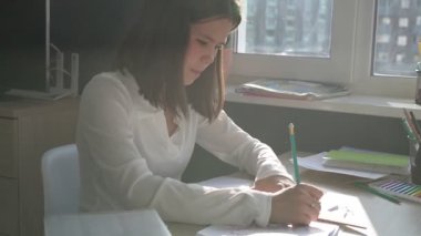 Evde eğitim gören liseli kız. Kız ders kitaplarıyla masada oturup ödev yapıyor.