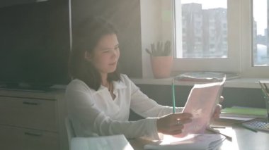 Evde eğitim gören liseli kız. Kız ders kitaplarıyla masada oturup ödev yapıyor.