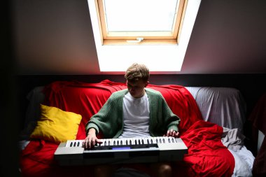 Genç adam synthesizer çalıyor, müzisyen evdeki kanepede oturan klavyede şarkı besteliyor.