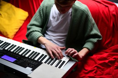 Genç adam synthesizer çalıyor, müzisyen evdeki kanepede oturan klavyede şarkı besteliyor.