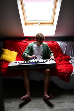 Genç adam synthesizer çalıyor, müzisyen evdeki kanepede oturan klavyede şarkı besteliyor.