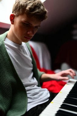 Genç adam synthesizer çalıyor, müzisyen evdeki kanepede oturan klavyede şarkı besteliyor.