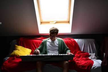 Genç adam synthesizer çalıyor, müzisyen evdeki kanepede oturan klavyede şarkı besteliyor.