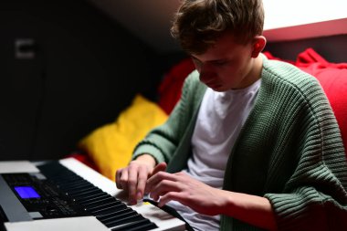 Genç adam synthesizer çalıyor, müzisyen evdeki kanepede oturan klavyede şarkı besteliyor.