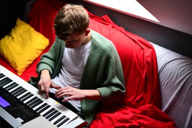 Genç adam synthesizer çalıyor, müzisyen evdeki kanepede oturan klavyede şarkı besteliyor.