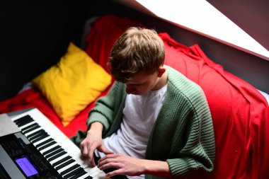 Genç adam synthesizer çalıyor, müzisyen evdeki kanepede oturan klavyede şarkı besteliyor.