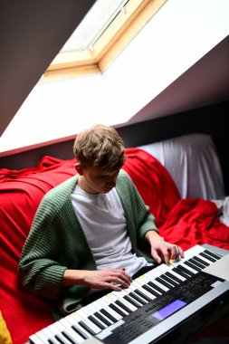 Genç adam synthesizer çalıyor, müzisyen evdeki kanepede oturan klavyede şarkı besteliyor.