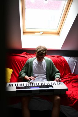 Genç adam synthesizer çalıyor, müzisyen evdeki kanepede oturan klavyede şarkı besteliyor.