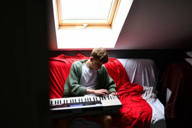 Genç adam synthesizer çalıyor, müzisyen evdeki kanepede oturan klavyede şarkı besteliyor.