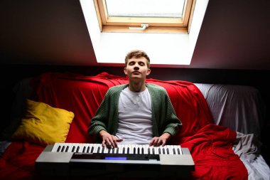 Genç adam synthesizer çalıyor, müzisyen evdeki kanepede oturan klavyede şarkı besteliyor.