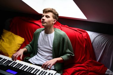 Genç adam synthesizer çalıyor, müzisyen evdeki kanepede oturan klavyede şarkı besteliyor.