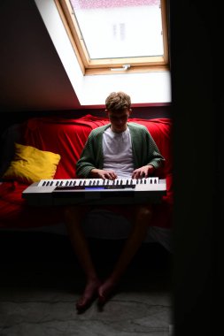 Genç adam synthesizer çalıyor, müzisyen evdeki kanepede oturan klavyede şarkı besteliyor.