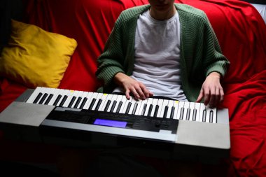 Genç adam synthesizer çalıyor, müzisyen evdeki kanepede oturan klavyede şarkı besteliyor.