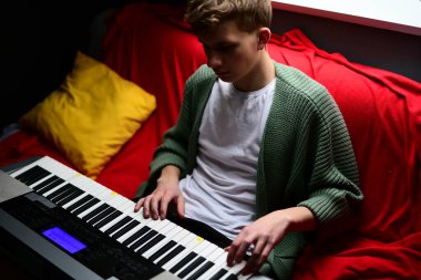 Genç adam synthesizer çalıyor, müzisyen evdeki kanepede oturan klavyede şarkı besteliyor.