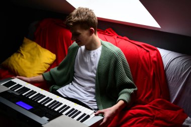 Genç adam synthesizer çalıyor, müzisyen evdeki kanepede oturan klavyede şarkı besteliyor.