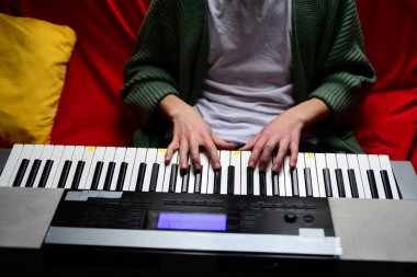 Genç adam synthesizer çalıyor, müzisyen evdeki kanepede oturan klavyede şarkı besteliyor.