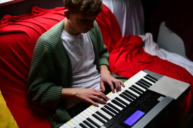 Genç adam synthesizer çalıyor, müzisyen evdeki kanepede oturan klavyede şarkı besteliyor.