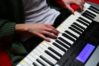 Genç adam synthesizer çalıyor, müzisyen evdeki kanepede oturan klavyede şarkı besteliyor.