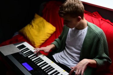 Genç adam synthesizer çalıyor, müzisyen evdeki kanepede oturan klavyede şarkı besteliyor.