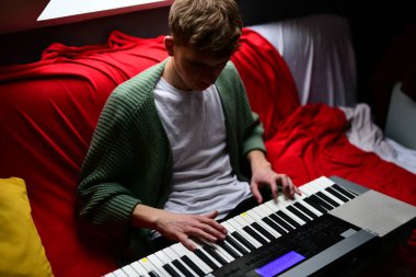 Genç adam synthesizer çalıyor, müzisyen evdeki kanepede oturan klavyede şarkı besteliyor.