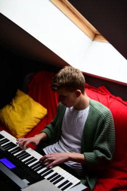 Genç adam synthesizer çalıyor, müzisyen evdeki kanepede oturan klavyede şarkı besteliyor.