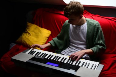 Genç adam synthesizer çalıyor, müzisyen evdeki kanepede oturan klavyede şarkı besteliyor.