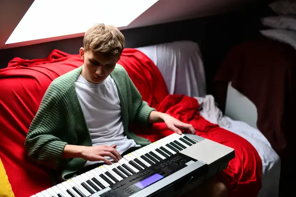 Genç adam synthesizer çalıyor, müzisyen evdeki kanepede oturan klavyede şarkı besteliyor.