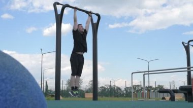 Beyaz tenli erkek sporcu, yaz parkında barfiks çekiyor.