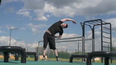Bir erkek sporcu dışarıda spor alanında antrenman yapıyor. Beyaz erkek sporcu yaz parkında antrenman yapmadan önce ısınma egzersizi yapıyor.