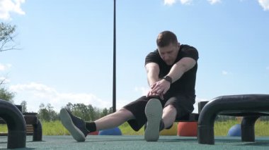 Bir erkek sporcu dışarıda spor alanında antrenman yapıyor. Beyaz erkek sporcu yaz parkında antrenman yapmadan önce ısınma egzersizi yapıyor.