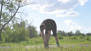 Bir erkek sporcu dışarıda spor alanında antrenman yapıyor. Beyaz erkek sporcu yaz parkında antrenman yapmadan önce ısınma egzersizi yapıyor.