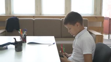 Evde eğitim görmüş bir öğrenci ev ödevini yapar. Çocuk ders kitapları ve renkli kalemlerle masada oturuyor.