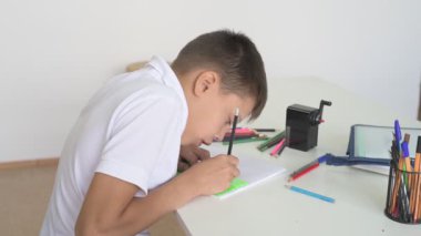 Evde eğitim görmüş bir öğrenci ev ödevini yapar. Çocuk ders kitapları ve renkli kalemlerle masada oturuyor.