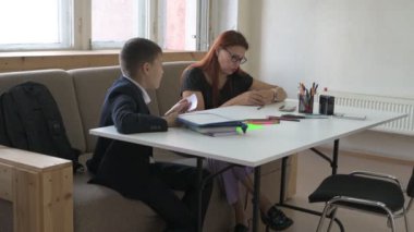 Evde eğitim görmüş bir çocuk ödevini masada annesiyle yapıyor. Çocuk evde bir öğretmenle ders çalışıyor.