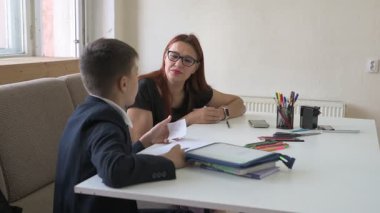 Evde eğitim görmüş bir çocuk ödevini masada annesiyle yapıyor. Çocuk evde bir öğretmenle ders çalışıyor.