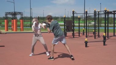 Sporcu erkek ve kız dışarıda boks antrenmanı yapıyorlar.