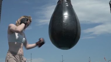 Profesyonel boksör kız dışarıda kum torbasını yumrukluyor.