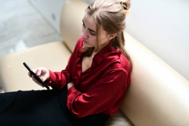 Evdeki kanepede elinde cep telefonuyla oturan genç bir kadın.