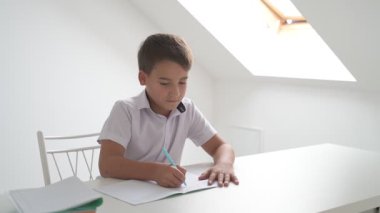 Küçük okul çocuğu ödev yapıyor, kalemle deftere yazıyor.