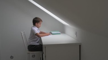 Küçük okul çocuğu ödev yapıyor, kalemle deftere yazıyor.