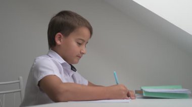 Küçük okul çocuğu ödev yapıyor, kalemle deftere yazıyor.