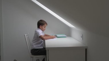 Küçük okul çocuğu ödev yapıyor, kalemle deftere yazıyor.