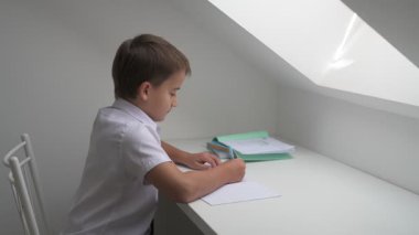 Küçük okul çocuğu ödev yapıyor, kalemle deftere yazıyor.